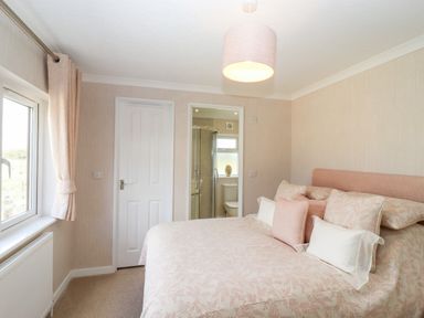 A bedroom with a bed and pillows next to a window and a door leading to a bathroom at 12 Bucklesham Park in Bucklesham near Trimley St Martin