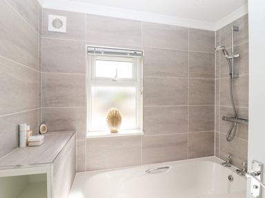 A bathroom with a bathtub shower and a window with a shell decoration at 12 Bucklesham Park Bucklesham near Trimley St Martin
