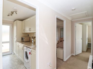 A hallway leading to a kitchen with washing machine microwave and cupboards and doors to other rooms at 12 Bucklesham Park in Bucklesham near Trimley St Martin