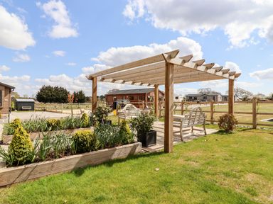 An outdoor seating area with wooden pergola and benches near planted garden beds at 12 Bucklesham Park in Bucklesham near Trimley St Martin