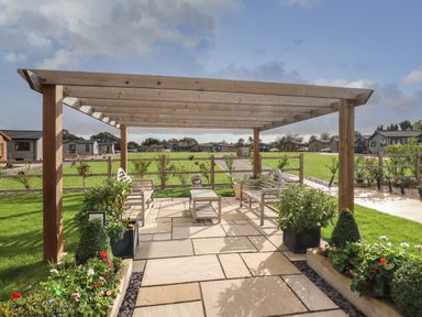 An outdoor seating area with wooden benches and a table under a wooden pergola surrounded by plants and grass at 12 Bucklesham Park in Bucklesham near Trimley St Martin