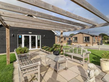 An outdoor patio area with wooden benches and a table under a wooden pergola near residential buildings at 12 Bucklesham Park in Bucklesham near Trimley St Martin
