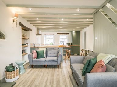A living room with two grey sofas and cushions and a kitchen with stools at Turn Cottage in Satterthwaite near Hawkshead