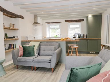 A living area with two grey sofas and green and pink cushions next to a kitchen with green cabinets and wooden stools at Turn Cottage in Satterthwaite near Hawkshead