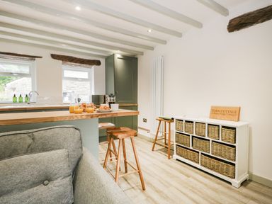 A kitchen area with wooden stools and breakfast on the counter next to a storage unit with woven baskets at Turn Cottage in Satterthwaite near Hawkshead