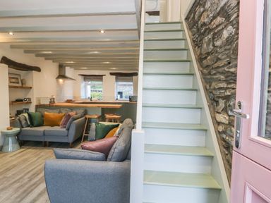 A living room with gray sofas and colorful cushions next to stairs and an open kitchen at Turn Cottage in Satterthwaite near Hawkshead