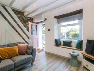 A living room with a gray sofa cushions a pink door window seat with cushions a small blue stool and a television at Turn Cottage in Satterthwaite near Hawkshead