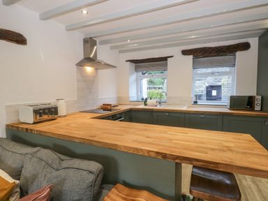 A kitchen with wooden countertops green cabinets a toaster kettle microwave two windows and a cooking area with an extractor hood at Turn Cottage in Satterthwaite near Hawkshead