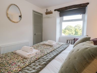 A bedroom with a bed, folded towels, a window with a view of trees, a mirror on the wall, and a closet at Turn Cottage in Satterthwaite near Hawkshead