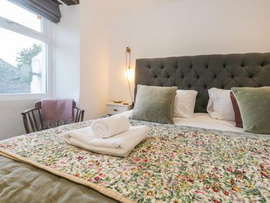 A bedroom with a bed with a floral quilt and pillows next to a window and a wooden chair at Turn Cottage in Satterthwaite near Hawkshead