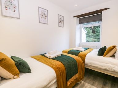 A bedroom with two single beds with pillows towels and blankets and a window with a view of trees at Turn Cottage in Satterthwaite near Hawkshead