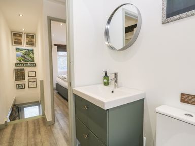 A small bathroom with a sink and mirror next to a hallway with stairs and a door to a bedroom at Turn Cottage in Satterthwaite near Hawkshead