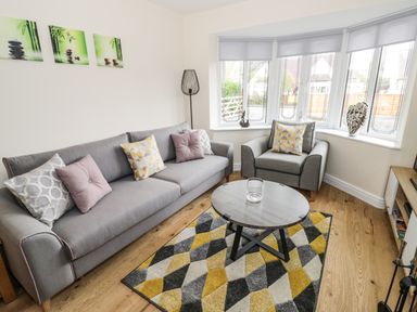A living room with gray sofa and armchair yellow and gray rug and round coffee table at Globe Cottage in Stratford-Upon-Avon