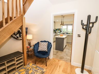 An entrance area with a wooden staircase a blue chair with a pillow a side table with a lamp and a door leading to a kitchen at Globe Cottage in Stratford-Upon-Avon