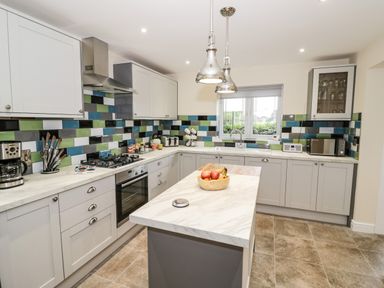 A kitchen with grey cabinets a marble island and colorful tile backsplash at Globe Cottage in Stratford-Upon-Avon