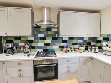 A kitchen with white cabinets multicolored tiled backsplash and countertop appliances at Globe Cottage in Stratford-Upon-Avon
