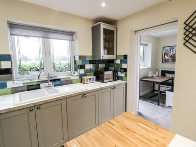 A kitchen with a sink microwave and colorful tiled backsplash next to a dining area with table and chairs at Globe Cottage in Stratford-Upon-Avon
