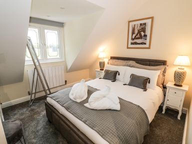 A bedroom with a bed two bedside tables with lamps a window and a full-length mirror at Globe Cottage in Stratford-Upon-Avon