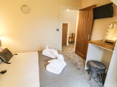 A bedroom with a bed a vanity table a tv on the wall and a wooden door at Globe Cottage in Stratford-Upon-Avon