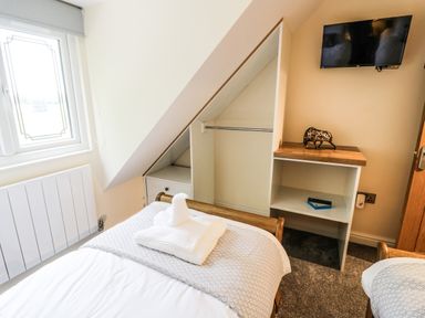 A bedroom with beds towels a wall mounted tv and an open closet at Globe Cottage in Stratford-Upon-Avon