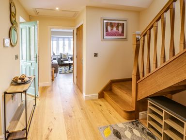 A hallway with wooden stairs a small bench a table with decorative items and an open door showing a living room at Globe Cottage in Stratford-Upon-Avon