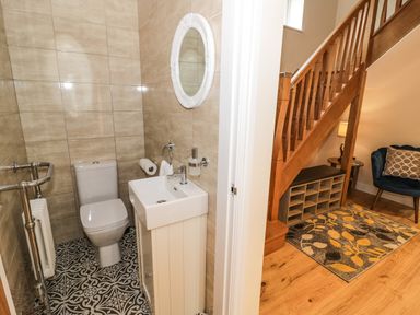 A small bathroom with a toilet sink and mirror next to a wooden staircase with seating and a patterned rug at Globe Cottage in Stratford-Upon-Avon