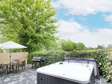 An outdoor patio with a hot tub dining table with chairs umbrella and a barbecue grill at Globe Cottage in Stratford-Upon-Avon