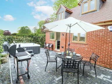 An outdoor patio with a barbecue grill a hot tub a table with four chairs and an umbrella at Globe Cottage in Stratford-Upon-Avon