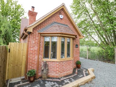 A small brick house with a bay window a chimney wooden gate potted plants and a statue near a pathway at Globe Cottage in Stratford-Upon-Avon