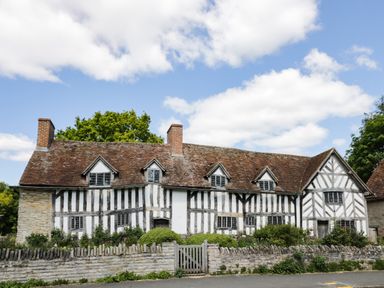 A half timbered cottage with a tiled roof surrounded by a stone wall and greenery at Globe Cottage in Stratford-Upon-Avon
