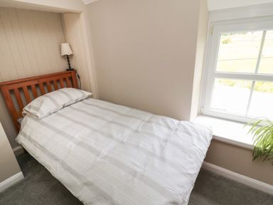 A bedroom with single bed with striped bedding a lamp on the headboard and a window at Maple Tree Cottage in Longframlington