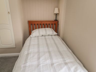 A single bed with striped bedding and a wooden headboard next to a wall lamp in a bedroom at Maple Tree Cottage in Longframlington