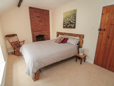 A bedroom with a bed wooden rocking chair and a brick fireplace at Maple Tree Cottage in Longframlington