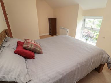 A bedroom with a bed with pillows and a window with a plant on the sill at Maple Tree Cottage in Longframlington