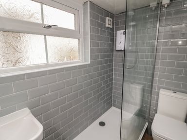 A bathroom with a shower enclosure, a toilet, a sink, and a frosted glass window at Maple Tree Cottage in Longframlington