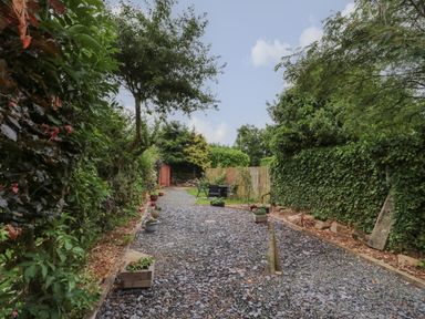 A garden path with potted plants on both sides and outdoor seating near a wooden shed at Maple Tree Cottage in Longframlington
