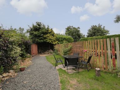 An outdoor garden area with a gravel path a wooden shed black chairs and table and wooden fence at Maple Tree Cottage in Longframlington