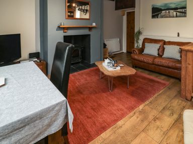 A living room with a brown leather sofa a wooden coffee table and a red rug at Maple Tree Cottage in Longframlington