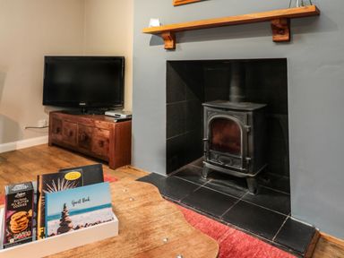 A wood burning stove in a fireplace with a television on a wooden cabinet and a wooden table with books and cookies at Maple Tree Cottage in Longframlington