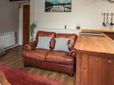 A brown leather loveseat with two gray pillows beside a wooden counter in a room with hardwood floors at Maple Tree Cottage in Longframlington
