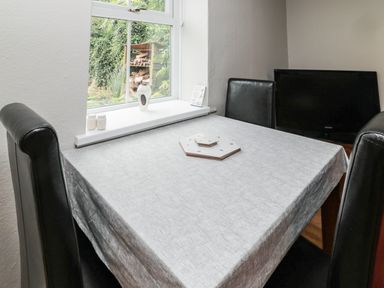 A small dining area with a table covered by a tablecloth surrounded by black chairs and a window showing a garden at Maple Tree Cottage in Longframlington