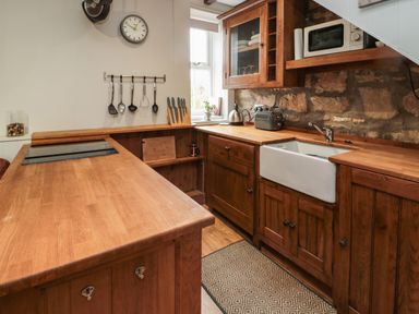 A kitchen with wooden cabinets a white sink a microwave and utensils on a wall at Maple Tree Cottage in Longframlington