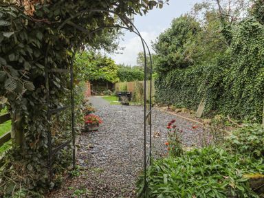 A gravel pathway with a metal arch and plants on the sides in a garden at Maple Tree Cottage in Longframlington