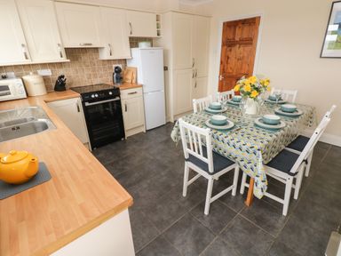 A kitchen with a dining table set for six with a vase of yellow flowers at Trem Y Morfa Newport Pembrokeshire