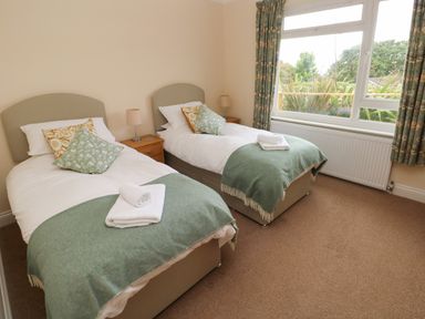 A bedroom with two single beds with green throws and pillows bedside tables and a large window at Trem Y Morfa in Newport Pembrokeshire