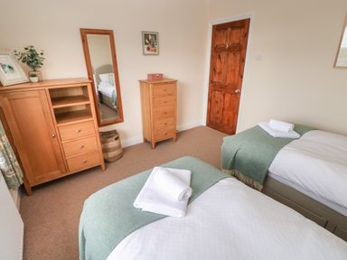 A bedroom with two single beds dressed with white linens and green blankets a wooden dresser a tall chest of drawers a standing mirror and a wooden door at Trem Y Morfa in Newport Pembrokeshire
