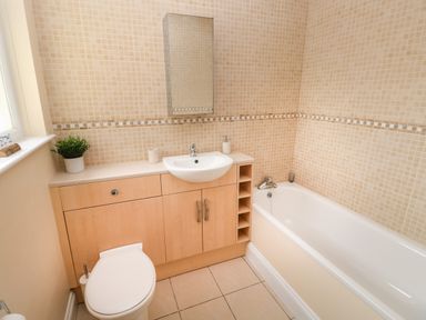 A bathroom with a wooden cabinet under a sink a toilet a bathtub and tiled walls at Trem Y Morfa in Newport Pembrokeshire