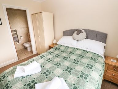 A bedroom with a bed with green patterned blanket and a stuffed sheep on the headboard at Trem Y Morfa in Newport Pembrokeshire