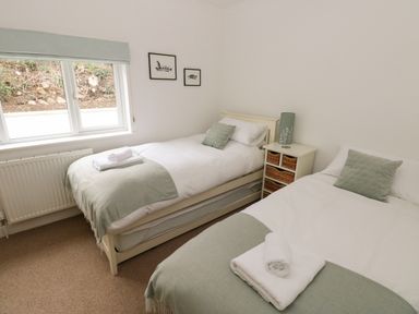 A bedroom with two single beds, green pillows, white linens, towels on each bed, a nightstand with baskets and a lamp between the beds, and a window on one side at Trem Y Morfa in Newport Pembrokeshire
