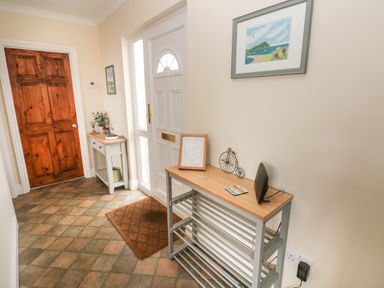 A hallway with a white front door a wooden shoe rack and a small table with decorations at Trem Y Morfa Newport Pembrokeshire